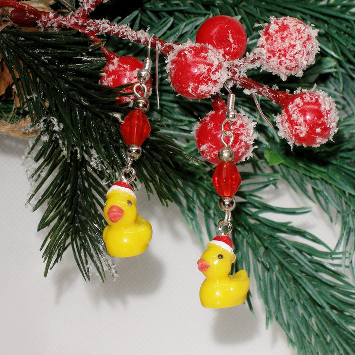 Christmas-themed earrings with red beads and rubber duck charms on a green pine branch.