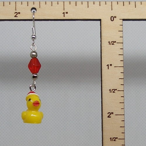 Yellow rubber duck and red bead earring with a ruler for scale on a gray background