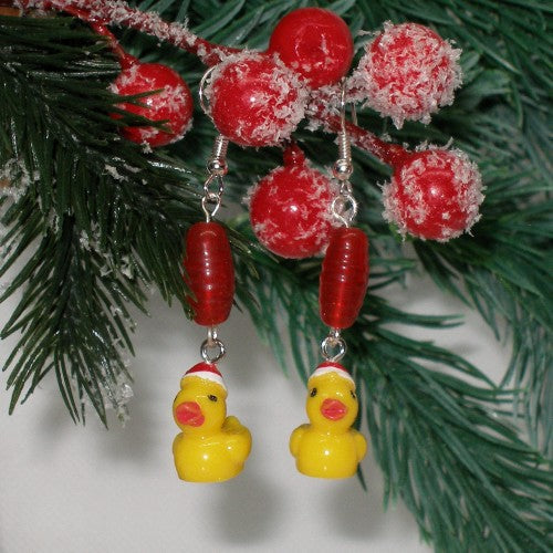 Decorative earrings with yellow rubber duck charms and red beads hanging on a Christmas tree branch.