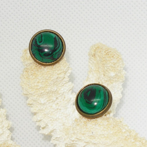 Green stone earrings with brass rims on a textured beige surface