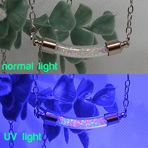 Necklace with clear cylindrical center and steel accents under normal light and UV light, with green leaves in the background.