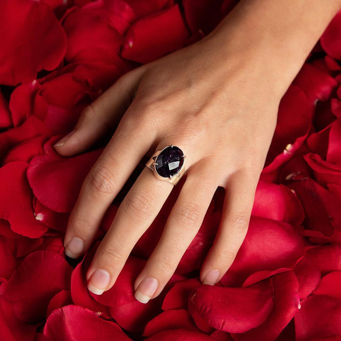 photo of a models hand wearing silver oval faceted amethyst ring on a bed of rose petals