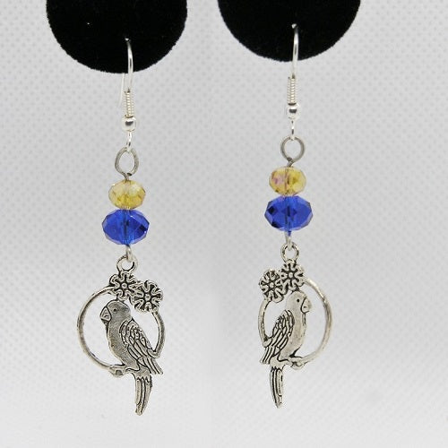 Pair of silver parrot-shaped earrings with blue and yellow beads on a gray background.