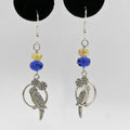 Pair of silver parrot-shaped earrings with blue and yellow beads on a gray background.