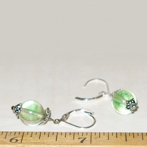 Pair of silver earrings with green beads on a white background, measured against a ruler.