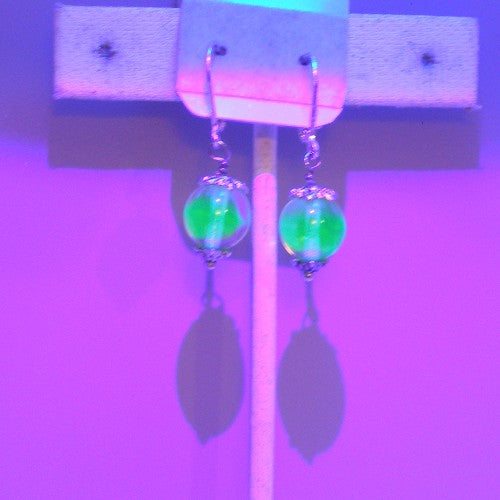 Green beaded earrings on a display card shown in Blacklight