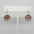 Colorful geometric patterned earrings on a white earring stand against a gray background