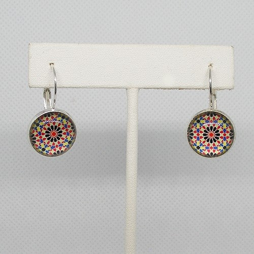 Colorful geometric patterned earrings on a white earring stand against a gray background