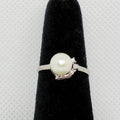 Pearl ring with crystal accents on a black stand against a gray background