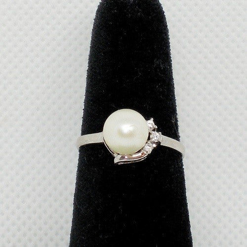 Pearl ring with crystal accents on a black stand against a gray background