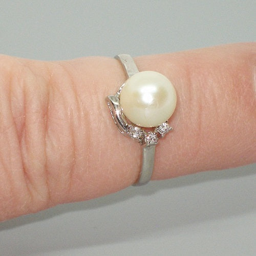 Pearl ring with silver band on a finger against a neutral background