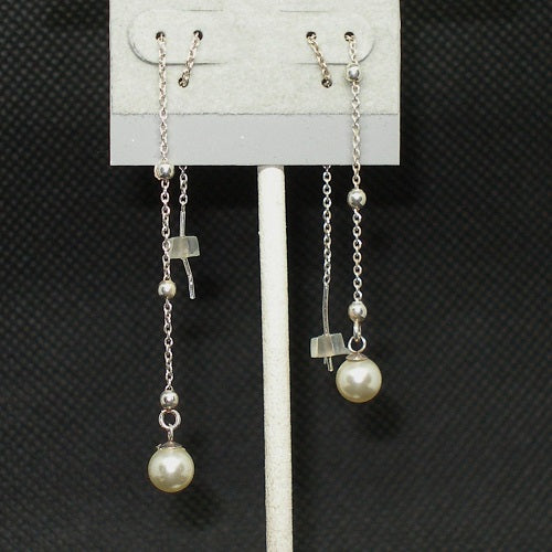 Pair of pearl threader earrings on a gray earring stand against a dark textured background