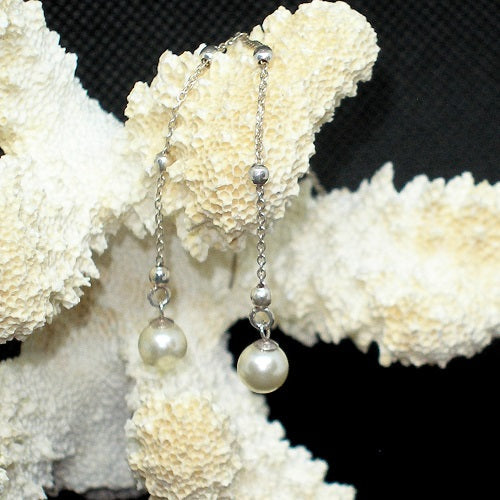 Pearl earrings hanging on a piece of coral with a black background