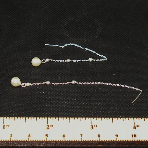 Pair of pearl earrings on a black background with a ruler for scale.