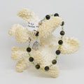 Green and Black beaded bracelet on a piece of coral against a white background