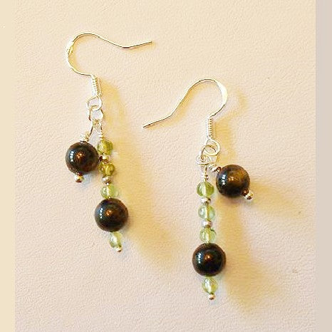 Pair of earrings with black and green beads on a beige background