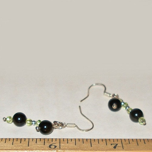 Pair of black and green beaded earrings on a white background with a ruler for scale.