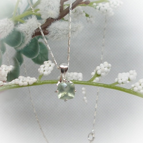 Silver necklace with a green gemstone pendant on a branch with white flowers