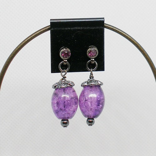 Purple beaded earrings with purple crystals on a black card against a white background