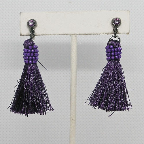 Purple tassel earrings on a white stand against a light gray background