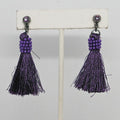Purple tassel earrings on a white stand against a light gray background