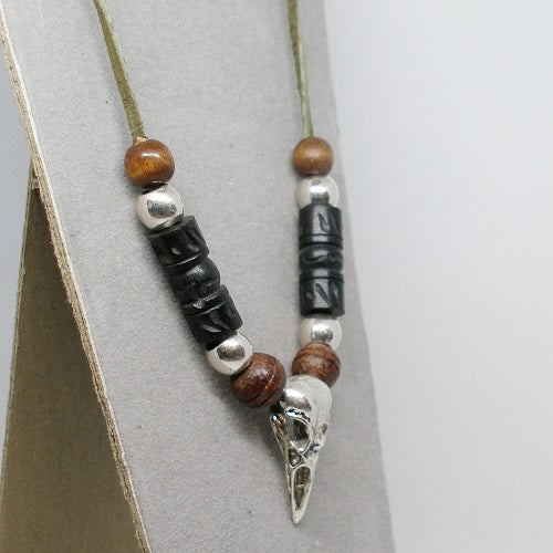 Beaded necklace with wooden and metal beads and a raven skull pendant on a gray background