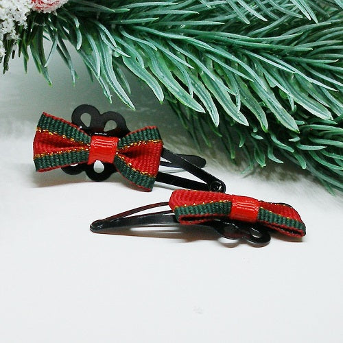 Red and green bow hair clips on a white surface with green leaves in the background