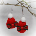 Red knitted earrings with white pom-poms and green bows on a branch background