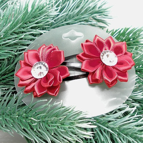 Red flower hair clips with a central gemstone on a clear background surrounded by green foliage.