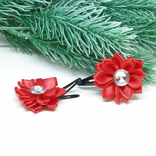 Red flower-shaped hair clips with a central gemstone on a white surface with green foliage in the background.