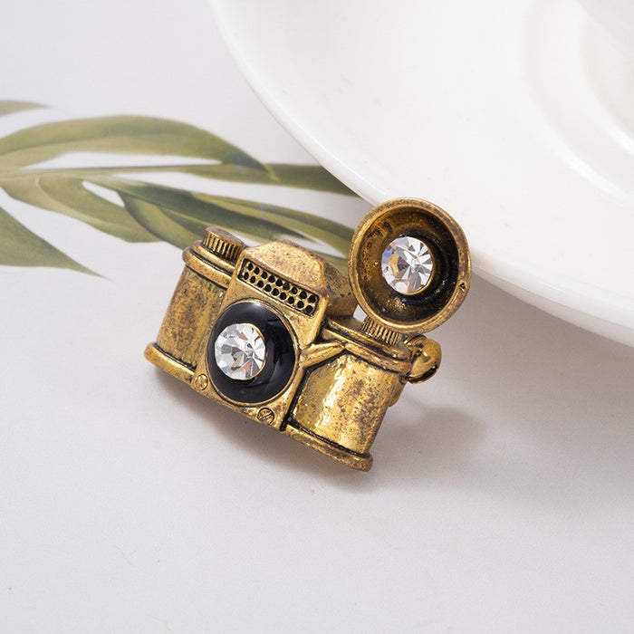 Vintage-inspired, playful, and full of character, the Retro Camera Brooch turns a classic camera silhouette into a stylish little statement piece. Featuring an antique gold-tone finish, sparkling crystal-style lens details, and a dimensional retro design, it adds a nostalgic touch to jackets, bags, scarves, and everyday outfits.