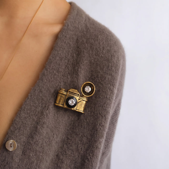 Vintage-inspired, playful, and full of character, the Retro Camera Brooch turns a classic camera silhouette into a stylish little statement piece. Featuring an antique gold-tone finish, sparkling crystal-style lens details, and a dimensional retro design, it adds a nostalgic touch to jackets, bags, scarves, and everyday outfits.
