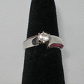 Silver ring with a white gem and ruby stones on a black stand against a gray background