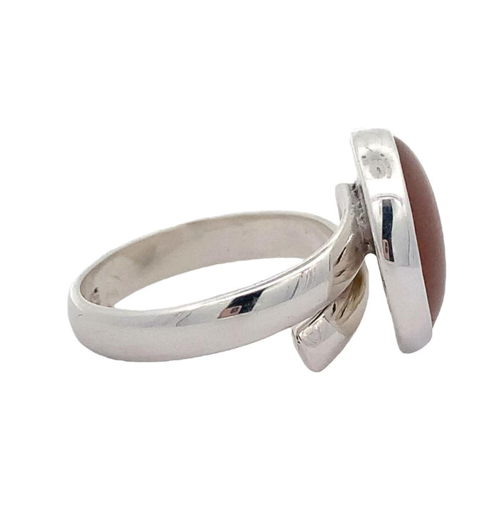 Photo of a round silver ring with a bezel set orange gem  on a white background side view