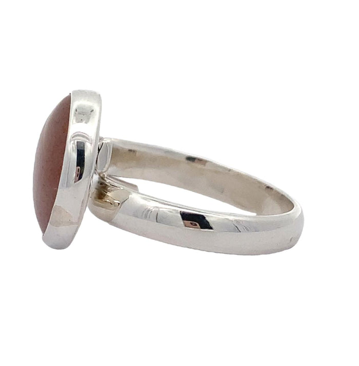 Photo of a round silver ring with a bezel set orange gem  on a white background Side view