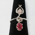 Silver ring with a red gemstone and zircon on a black stand against a white background
