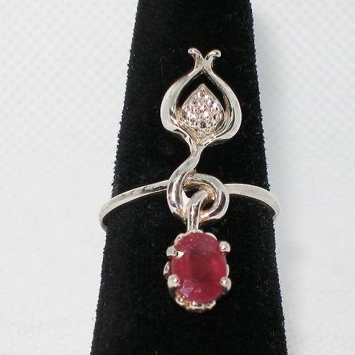 Silver ring with a red gemstone and zircon on a black stand against a white background