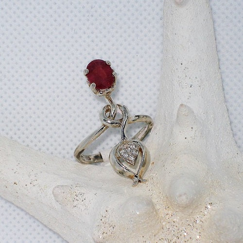 Silver ring with a red gemstone and small diamond like stones on a textured white surface