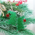 Green glittery Christmas tree earrings with red ornament on a branch.