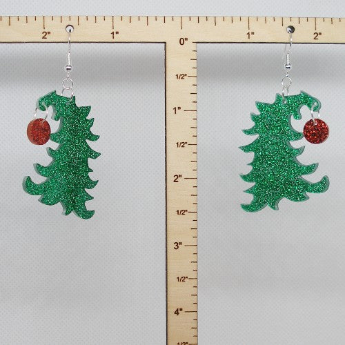 Green glittery Christmas tree earrings with red ornament on a gray background with a ruler for scale.