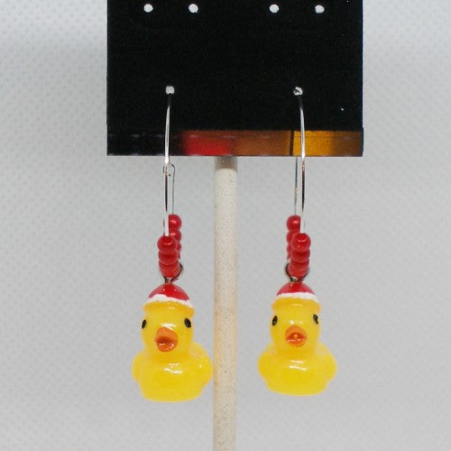 Yellow rubber duck earrings with red hats on a stand against a white background