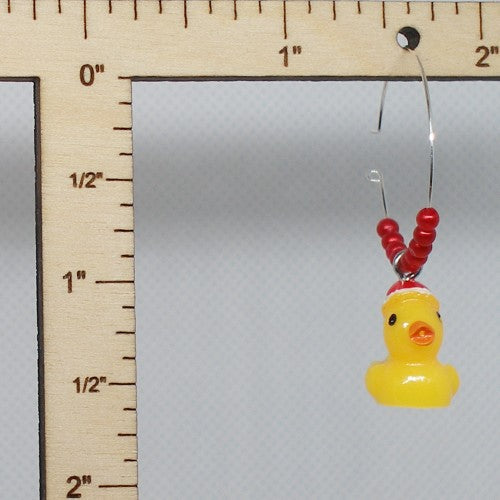 Yellow rubber duck Christmas earrings on a gray background with a ruler for scale.