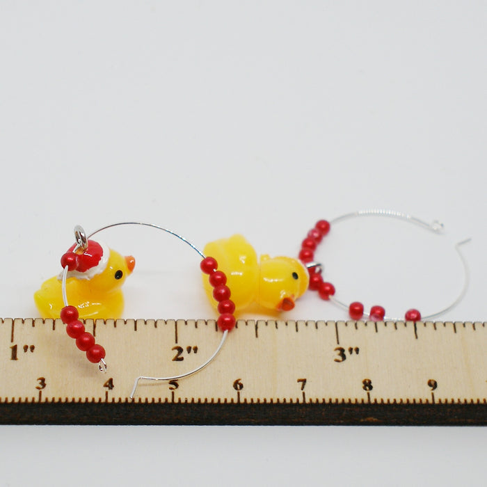 Two yellow rubber duck earrings with  red beads with a ruler for scale on a white background
