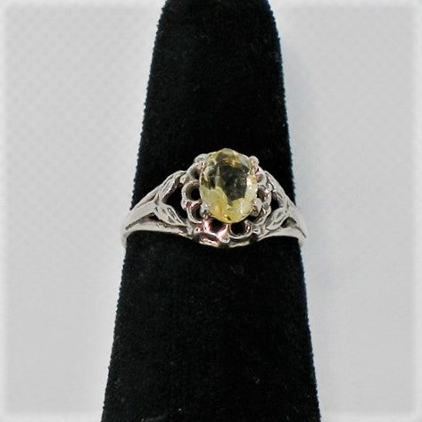 Silver ring with a yellow gemstone on a black velvet stand against a white background
