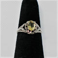 Silver ring with a yellow gemstone on a black velvet stand against a white background