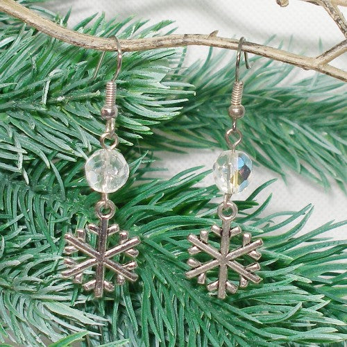 Silver snowflake earrings with clear beads on an evergreen branch.
