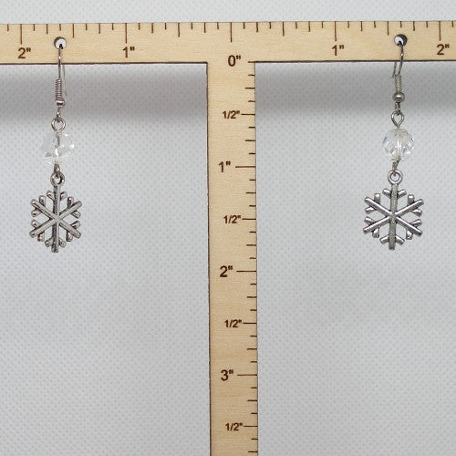 Silver snowflake earrings with clear beads on a ruler for scale.
