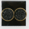 Pair of round earrings with black textured centers and gold borders on a black card.