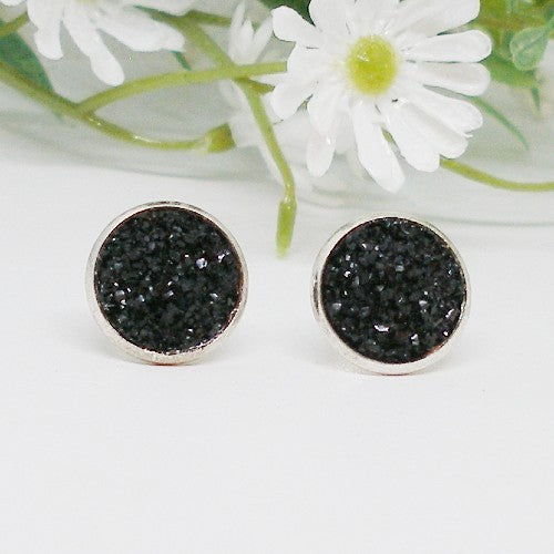 Black druzy stud earrings on a white background with white flowers.