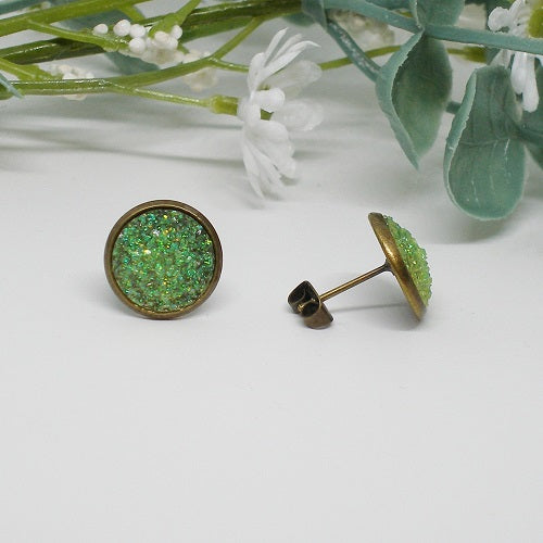 Green druzy stud earrings on a white surface with greenery in the background